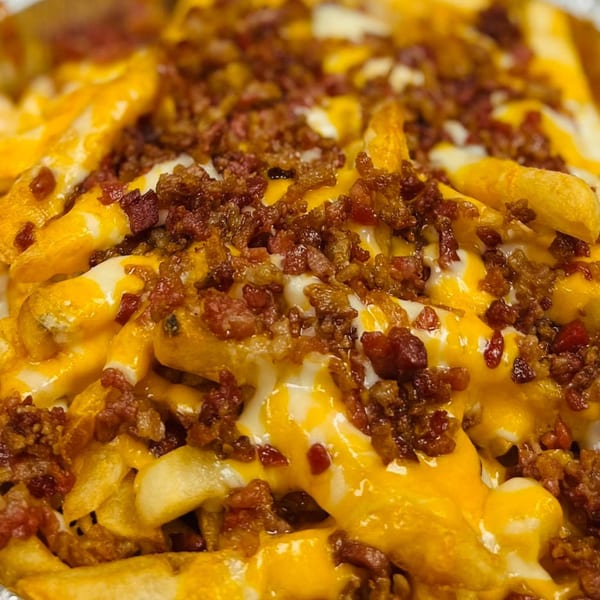 Close-up of Bonilla's Pizza loaded fries with melted cheese, white sauce, and crispy bacon bits.