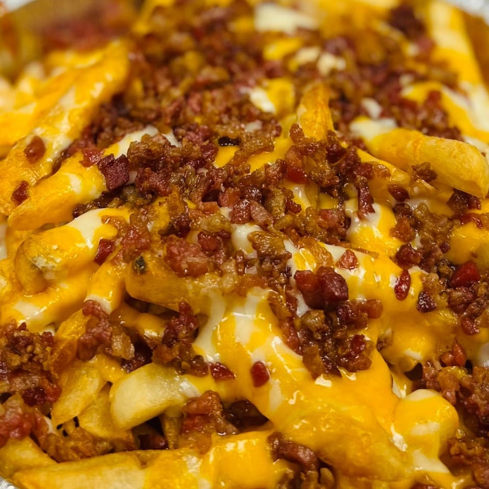 Close-up of Bonilla's Pizza loaded fries with melted cheese, white sauce, and crispy bacon bits.