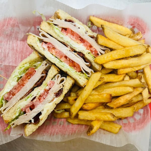 A club sandwich with turkey, bacon, lettuce, and tomato, served with a side of golden french fries.