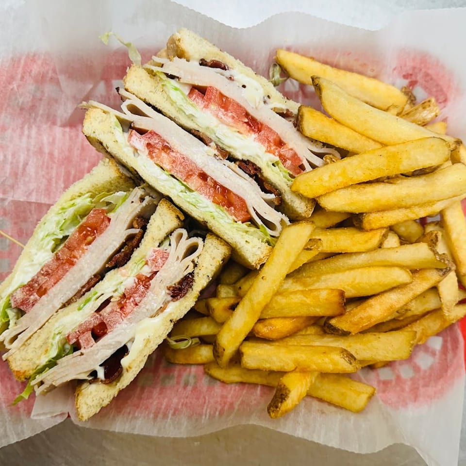 A club sandwich with turkey, bacon, lettuce, and tomato, served with a side of golden french fries.