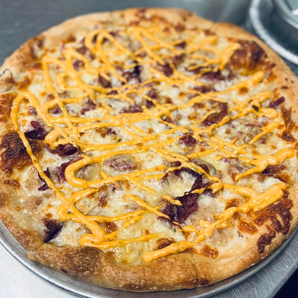 Bonilla's Pizza with white cheese, meat toppings, and a yellow sauce drizzle on a metal pan.